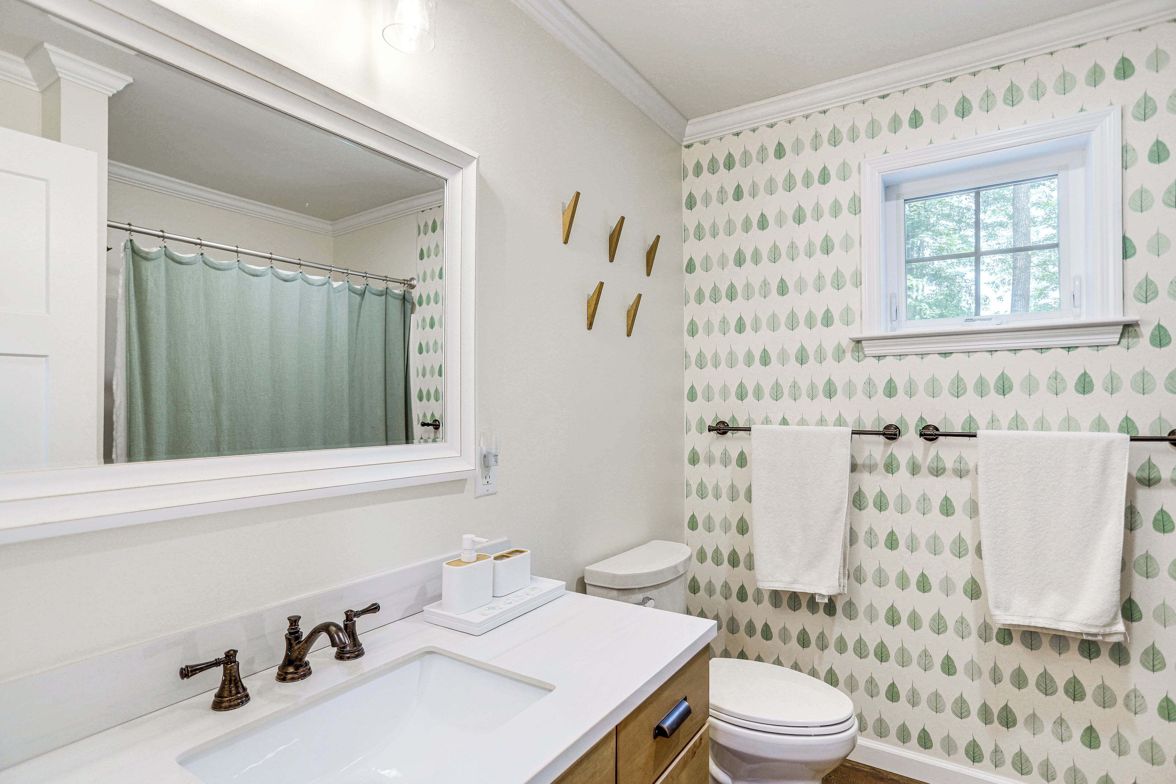 A bathroom with a white sink, a mirror, a toilet, and a window with a view of trees.