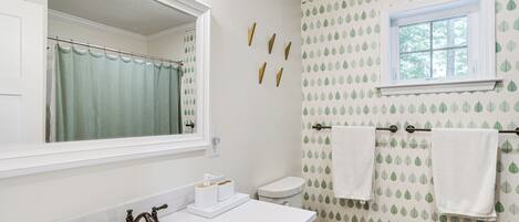 A bathroom with a white sink, a mirror, a toilet, and a window with a view of trees.