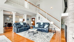 A spacious living room with a large blue sectional sofa, a round coffee table, and a fireplace. A staircase with a wooden railing leads to an upper level. - Waterfront Bliss: Wheeler Lake Retreat w/ Dock! (Athens)