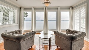 Une pièce comprenant deux fauteuils capitonnés, une table en verre et de grandes fenêtres avec des rideaux.
