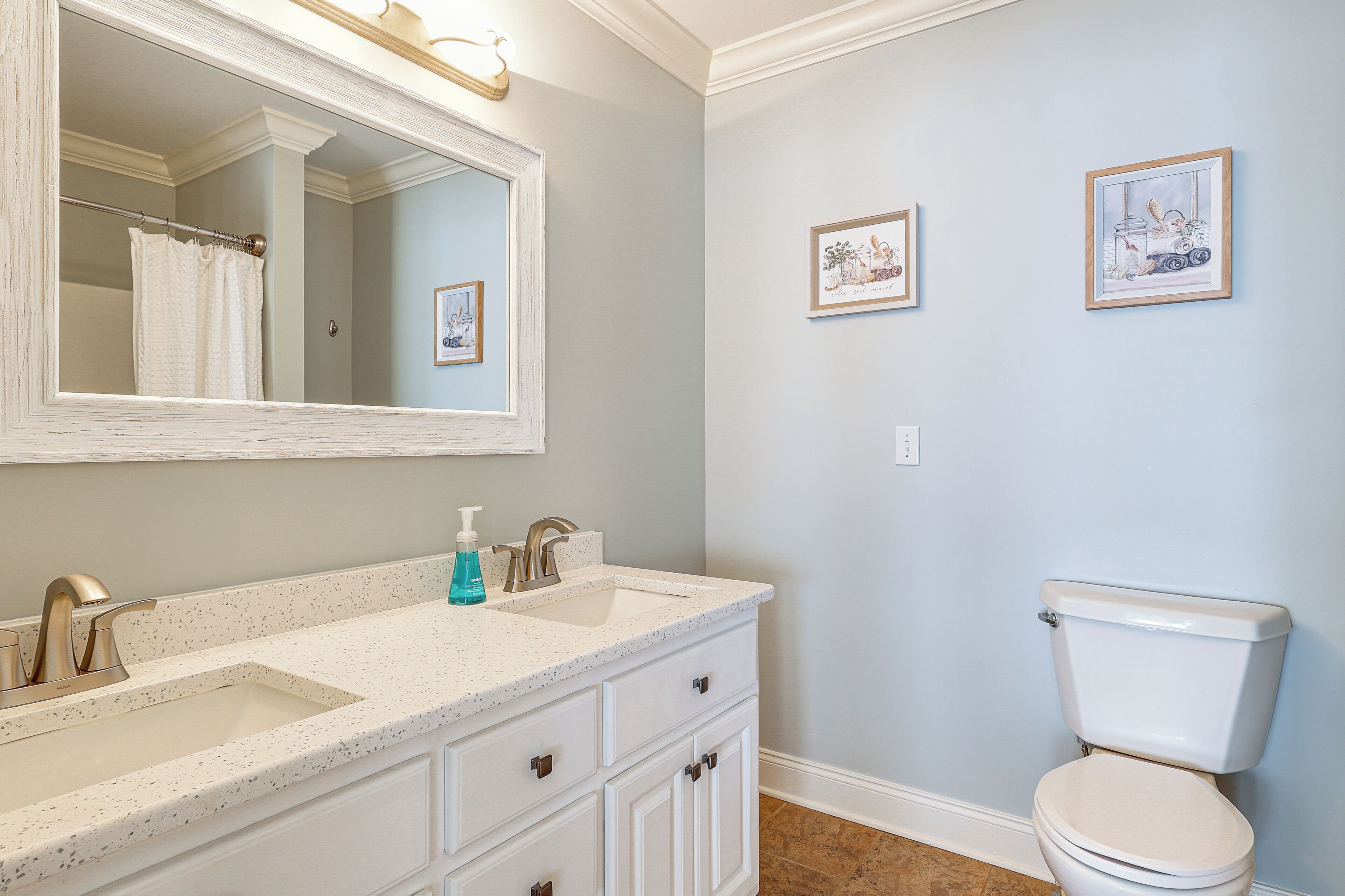 Une salle de bain avec un double lavabo, des toilettes et deux tableaux encadrés au mur.