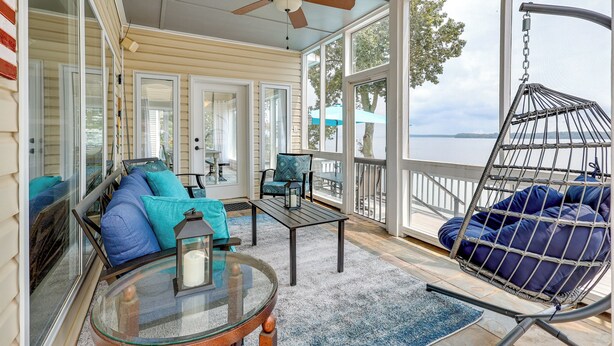 Une véranda avec une porte vitrée, un ventilateur de plafond, un fauteuil suspendu et une vue sur le lac.