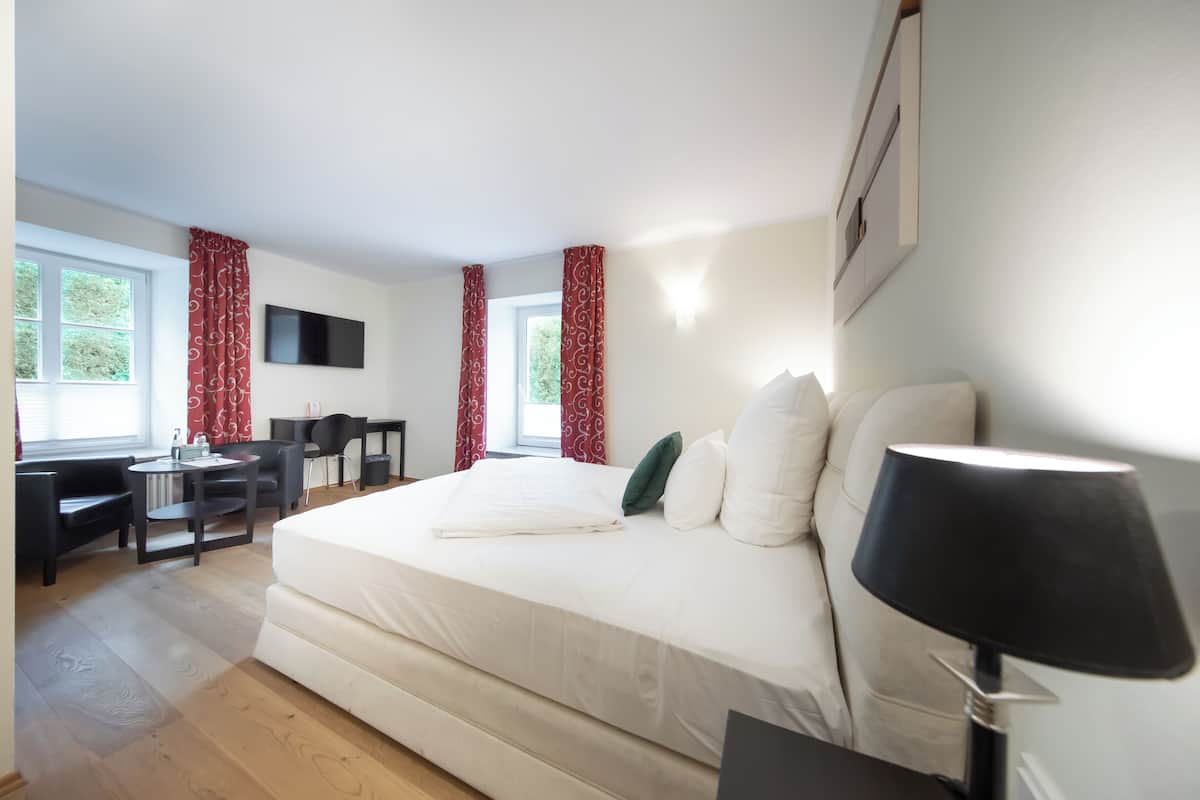 Una habitación de hotel con una cama grande, un escritorio con silla, un televisor montado en la pared y una ventana con cortinas.