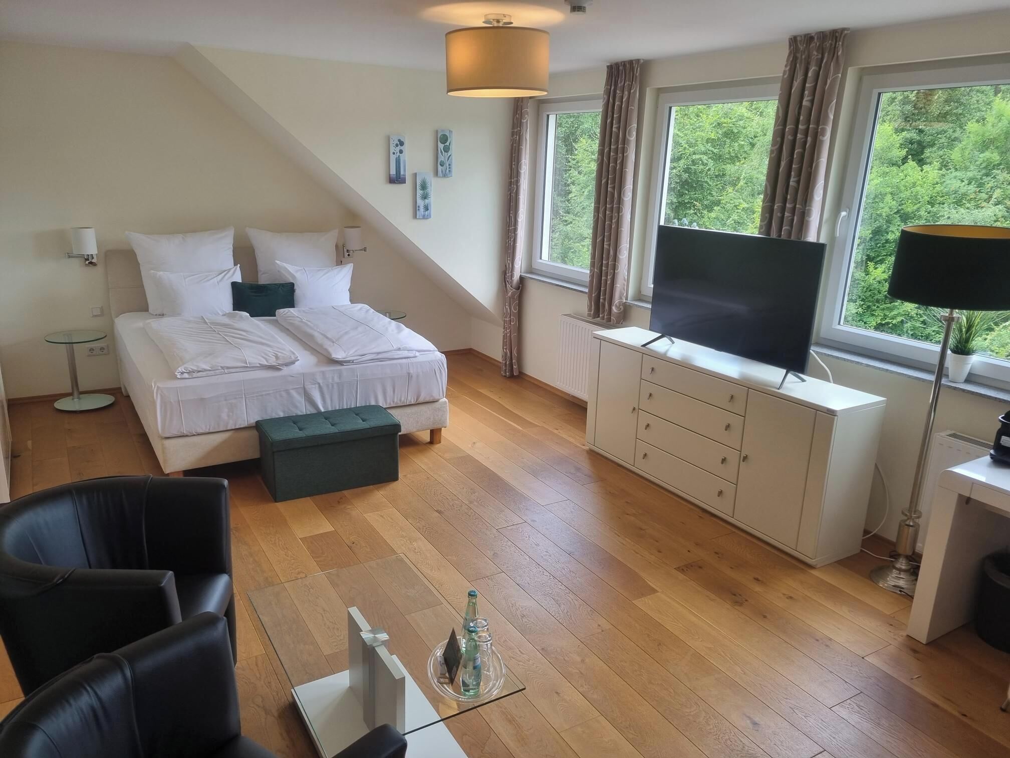 A modern bedroom with a bed, a TV, a desk, and a window with curtains.