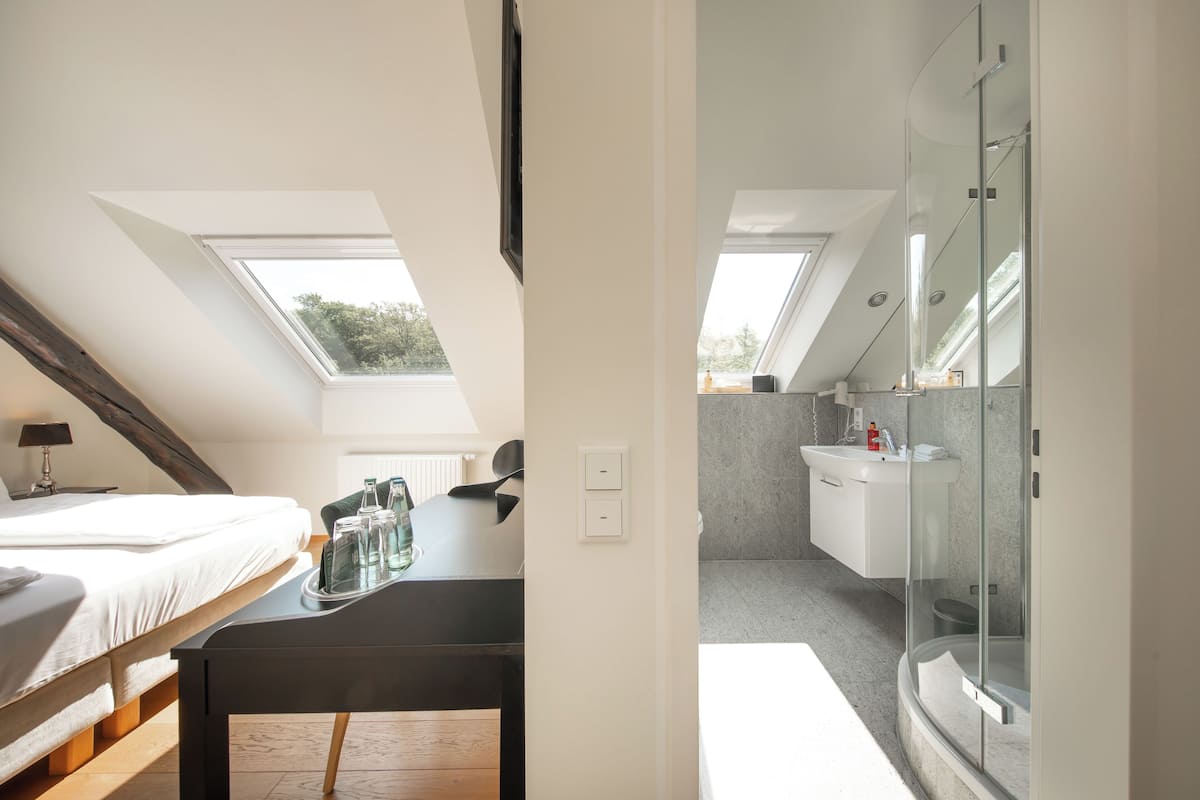Un dormitorio con tragaluz, una cama, un escritorio con una bandeja de botellas y vistas al exterior.