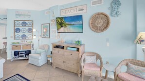 A beach-themed living room with a large TV, wicker furniture, and a sign that reads "BEACH 500 FT". - The Palms 714 by Liquid Life (Orange Beach)