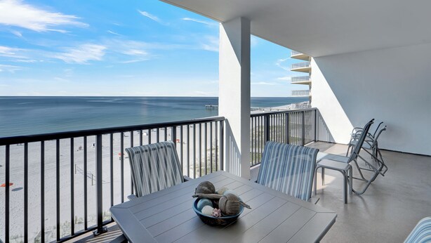 A balcony with a view of the ocean, a table with a bowl of items, and striped chairs. - The Palms 714 by Liquid Life (Orange Beach)