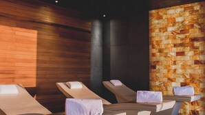 A spa area with three massage tables, each with a towel and a cushion. The room has wooden paneling on one wall and a stone wall on the other. - Al Faya Retreat by Sharjah Collection (Al Madam)