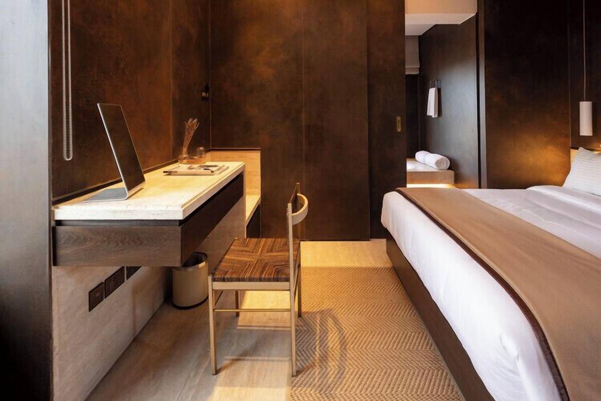 A modern hotel room with a large bed, a desk with a laptop, a chair, and a small table.