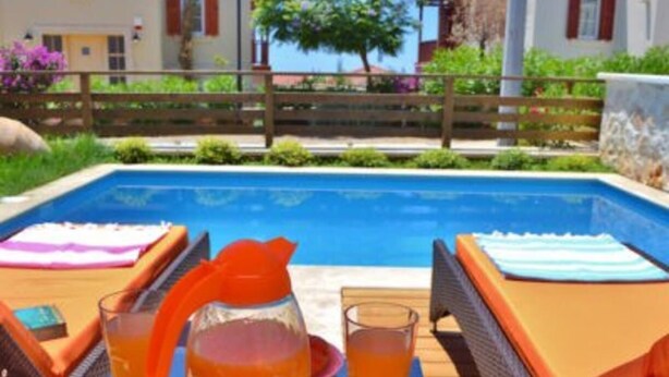 Ein Poolbereich mit Liegestühlen, einem Tisch mit Getränken und Blick auf einen Pool sowie Gebäude im Hintergrund.