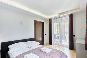 A hotel room with a bed, a door, a window with curtains, and a view of the outside.