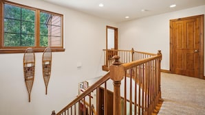 Una escalera con barandillas de madera y piso alfombrado, que conduce a una habitación con puerta de madera y ventana con vistas a la vegetación.