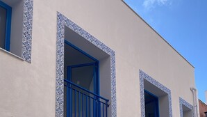 A building with a flat facade, multiple windows with blue frames, and a white fence.