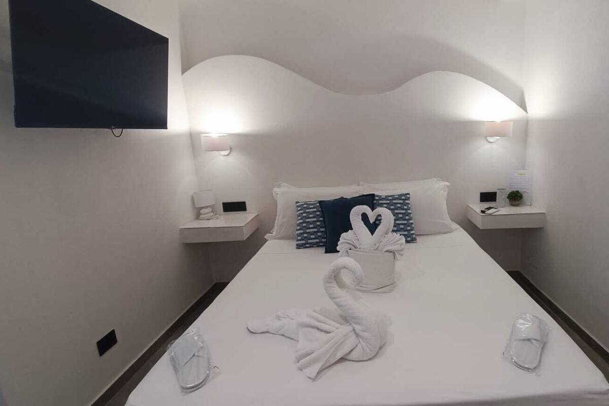 A hotel room with a neatly made bed, two bedside tables with lamps, and a flat-screen TV mounted on the wall.