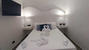 A hotel room with a neatly made bed, two bedside tables with lamps, and a flat-screen TV mounted on the wall.