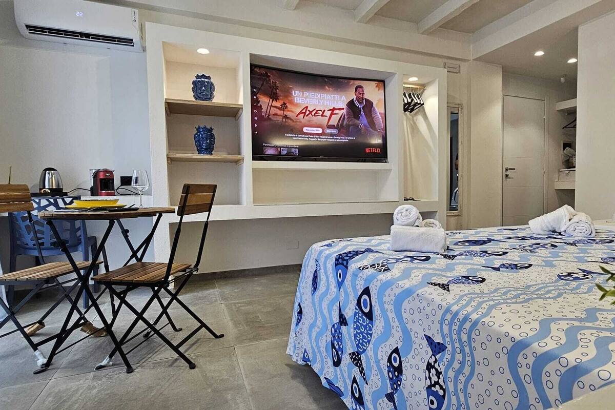 A hotel room with a bed, a desk with a chair, a television, and a potted plant.