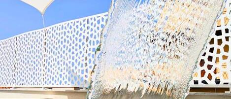 A water feature with a clear blue pool and a white, geometric fence in the background.