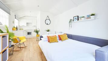 A modern, well-lit room with a bed, a sofa, a dining area, and a kitchen.