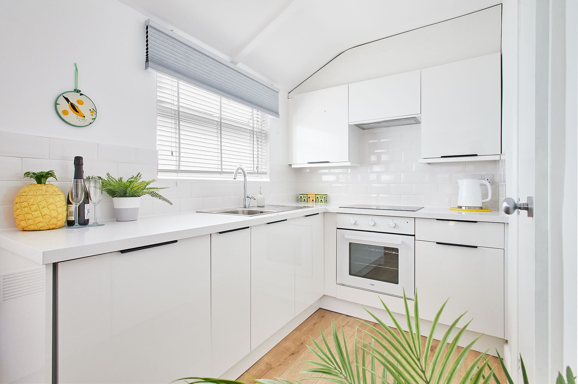 A modern kitchen with white cabinetry, a built-in oven, and a window with blinds.