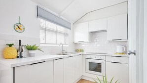 Een moderne keuken met witte kasten, een inbouwoven en een raam met jaloezieën.