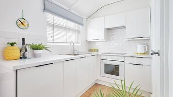 A modern kitchen with white cabinetry, a built-in oven, and a window with blinds.