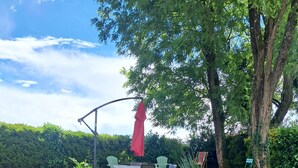 Un espacio al aire libre con césped, una mesa, sillas, un paraguas rojo y árboles.