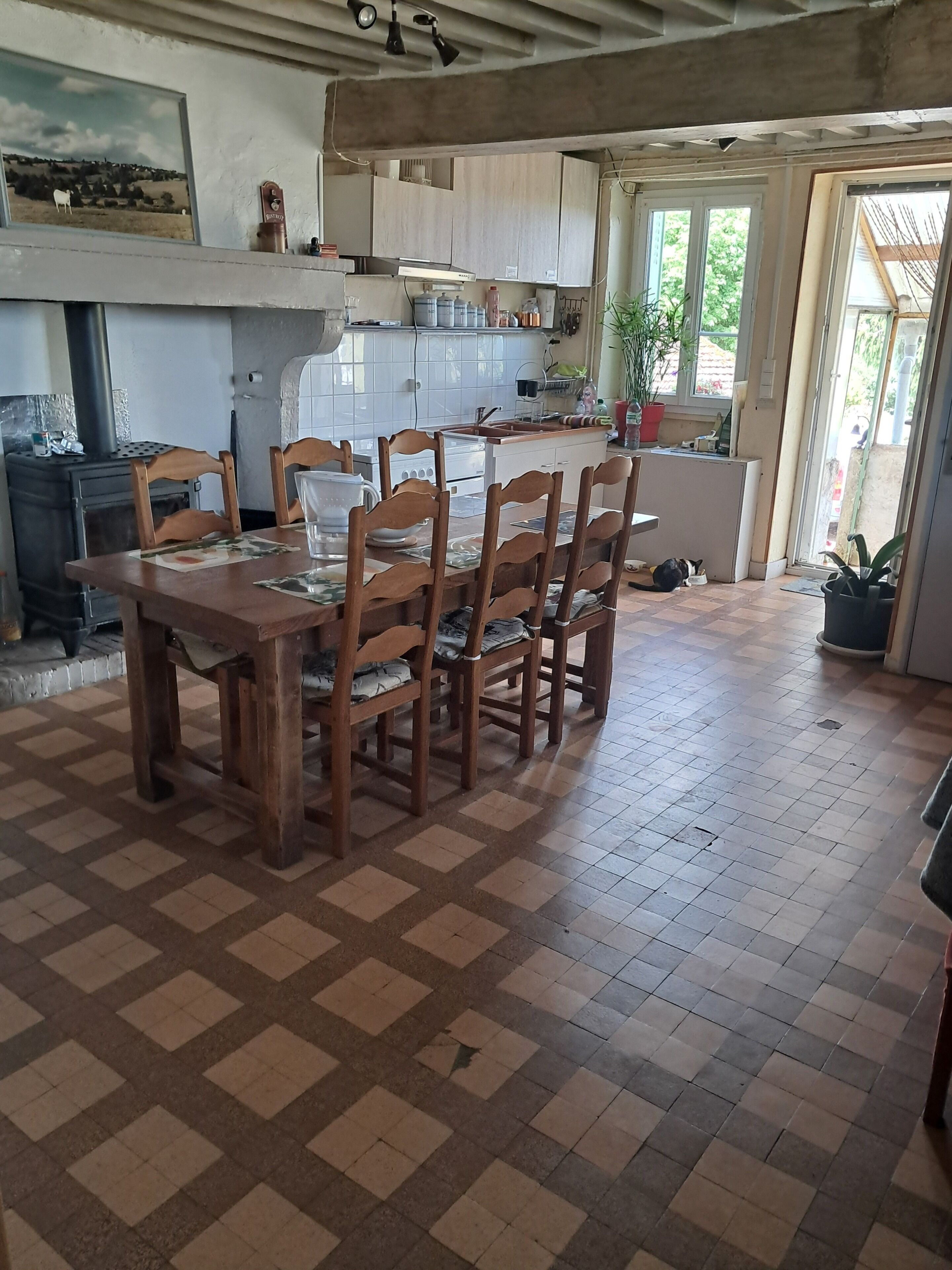 Un coin repas avec un sol à carreaux, des chaises en bois, une table et une cuisine en arrière-plan.