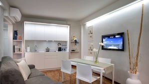 A modern kitchen with white cabinets, a dining area with a white table and chairs, and a TV mounted on the wall. - Butterfly Beachside Apartment (Viareggio)