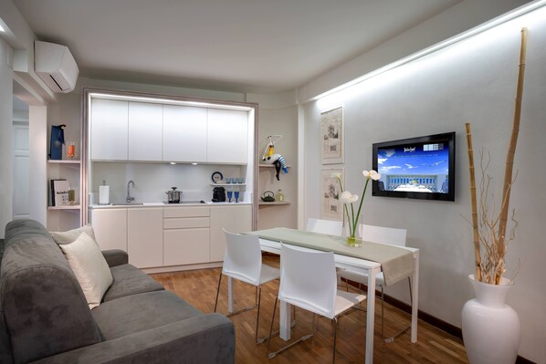 A modern kitchen with white cabinets, a dining area with a white table and chairs, and a TV mounted on the wall.