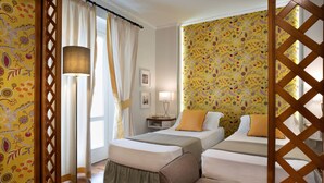 A hotel room with two beds, a bedside table, a lamp, and a window with curtains. - Butterfly Beachside Apartment (Viareggio)