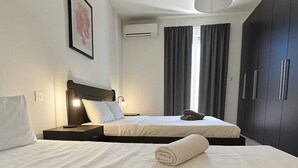 A hotel room with two beds, a dark wardrobe, a framed picture on the wall, and a window with curtains. - FUN GAME St. Julians Apartment 2 (St. Julians)