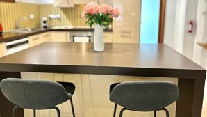 A modern kitchen with a central island, two grey chairs, and a vase with pink flowers. - FUN GAME St. Julians Apartment 2 (St. Julians)