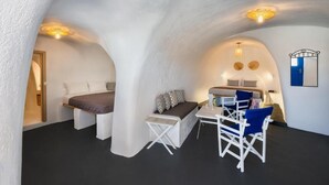 A cozy, well-lit room with a bed, a sofa, and a small table with chairs. - Blue Vice Imerovigli (Santorini)