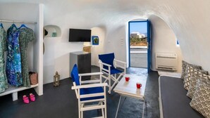 A compact room with a bed, a table with two red cups, a TV on the wall, and a view of the outside. - Blue Vice Imerovigli (Santorini)
