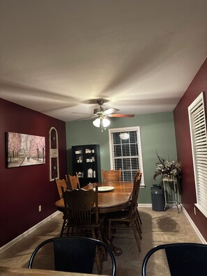 A dining area with a table, chairs, a ceiling fan, a window with blinds, and a decorative plant. - Whole house Los Flores  (Snow Hill)
