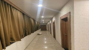 Un couloir bordé d’une rangée de portes en bois fermées, avec un sol carrelé et des murs de couleur beige.