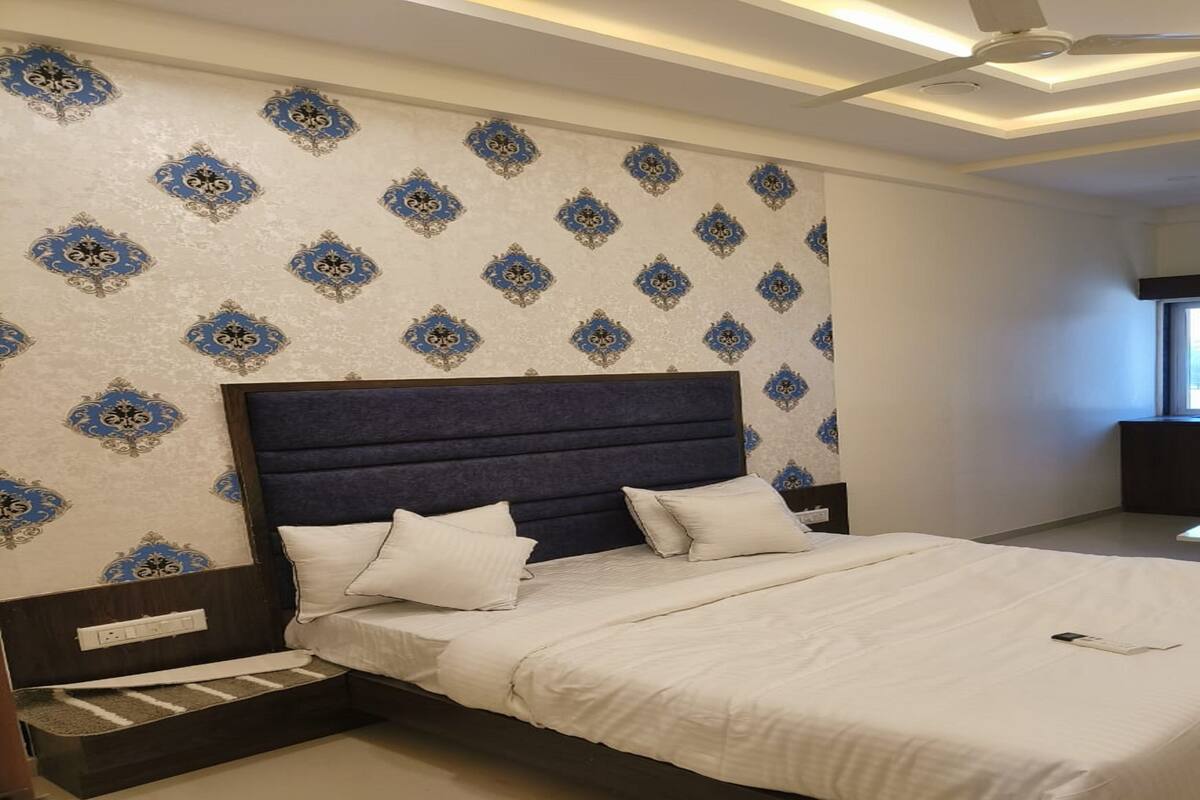 A bedroom with a large bed, a headboard, and patterned wallpaper.