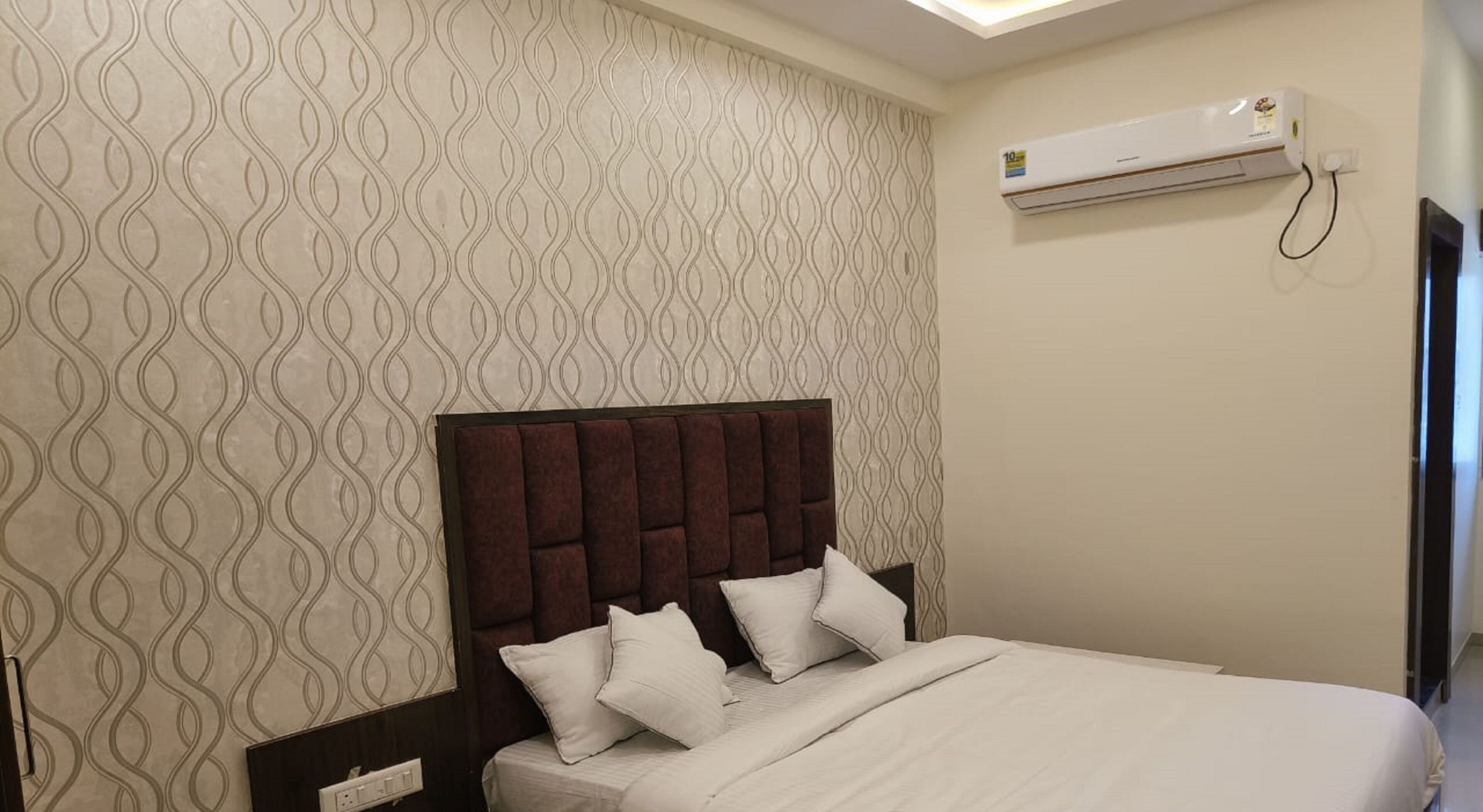 A hotel room with a patterned wallpaper, a bed with a dark headboard, and an air conditioning unit on the wall.