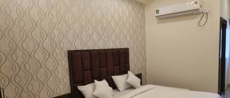 A hotel room with a patterned wallpaper, a bed with a dark headboard, and an air conditioning unit on the wall.