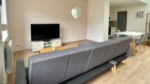 Ein modernes Wohnzimmer mit Flachbildfernseher, einer Couch und einem Essbereich mit Tisch und Stühlen.