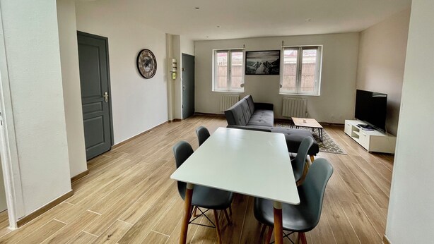 Ein modernes Wohnzimmer mit Essbereich, einem grauen Sofa, einem Flachbildfernseher und einem Gemälde an der Wand.