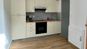 Eine kompakte Küche mit weißen Schränken, einem schwarzen Backofen, einem Edelstahl-Wasserkocher und einer Holz Arbeitsplatte.
