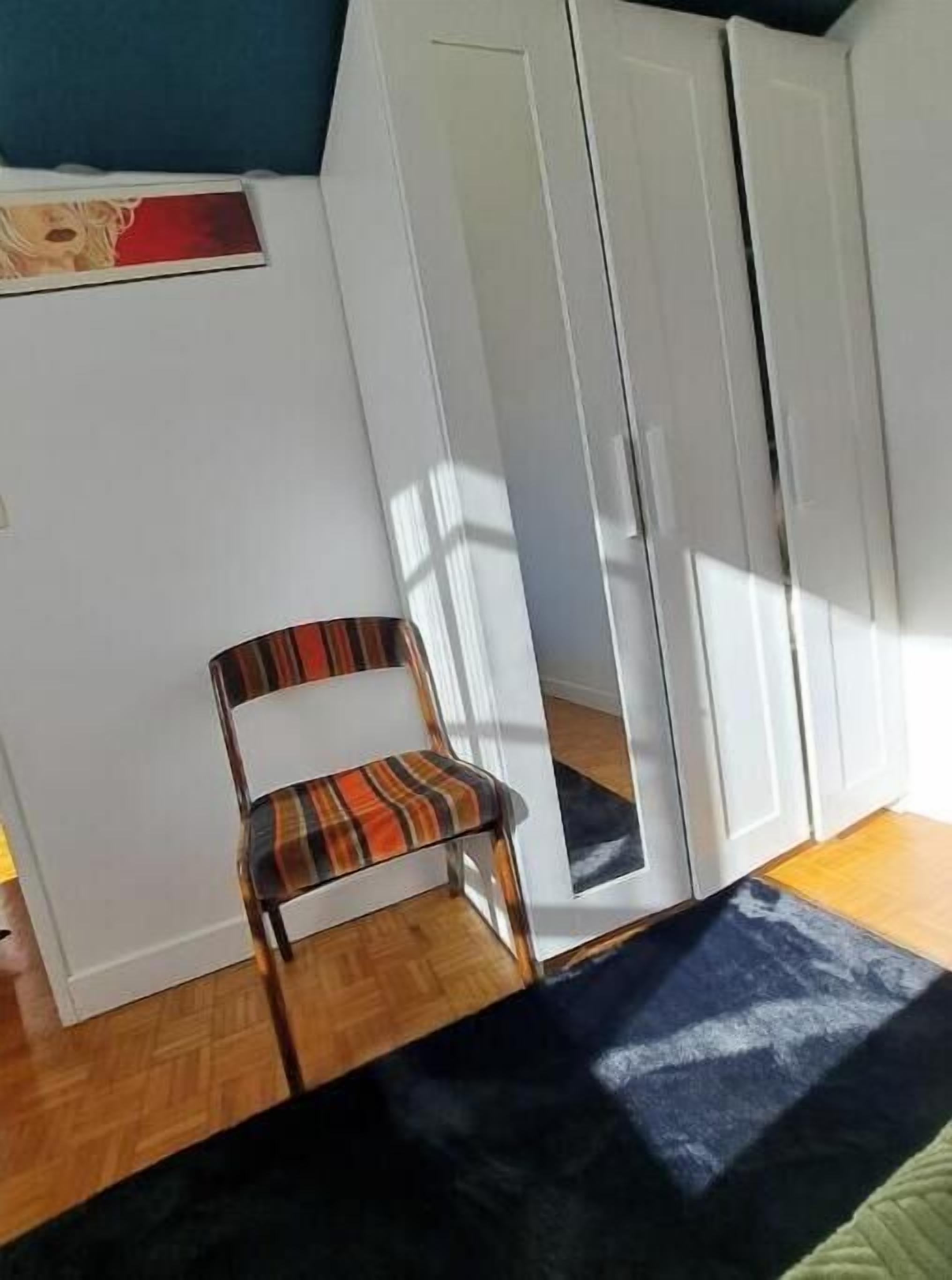 Una habitación con una silla de cuadros, una alfombra azul oscuro, suelo de madera y paredes blancas.