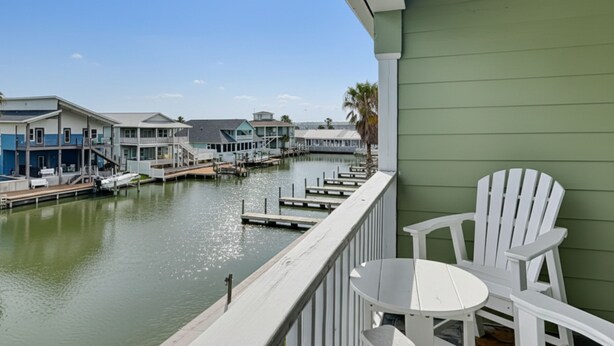 A waterfront property with a balcony, white Adirondack chairs, and a view of a marina with boats and buildings. - Kontiki Beach Resort #317 | Canal-Front View + Pool Access! (Rockport)