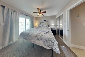 A bedroom with a bed, two bedside tables, a ceiling fan, and a view through a window.