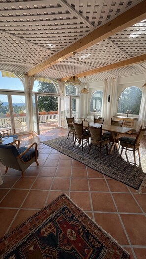 Une vaste terrasse dotée d’une table et de chaises en bois, d’un tapis à motifs et offrant une vue sur l’extérieur.