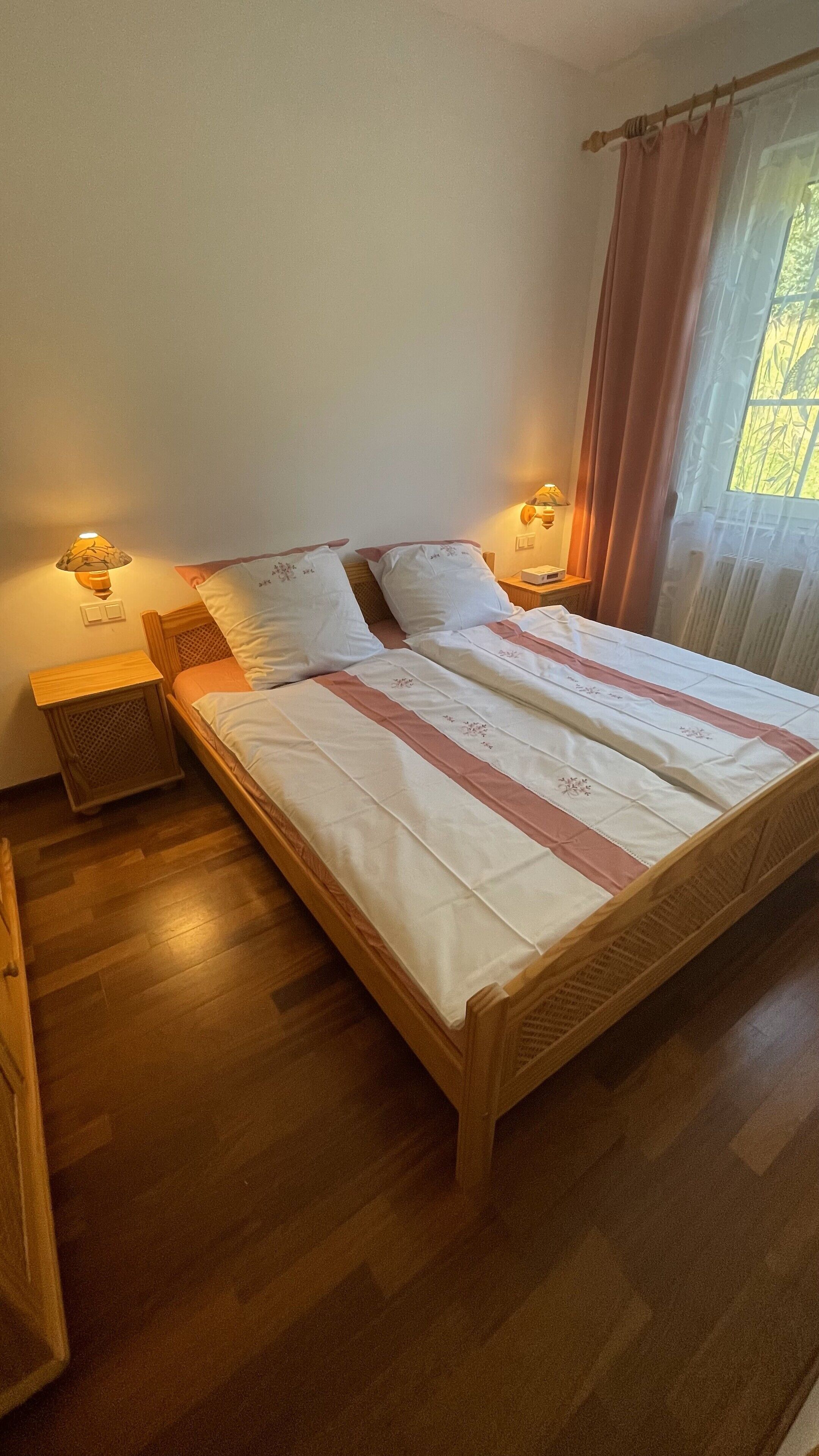 Ein ordentlich bezogenes Bett mit gestreifter Bettdecke, zwei Nachttischlampen und ein Fenster mit Vorhängen.