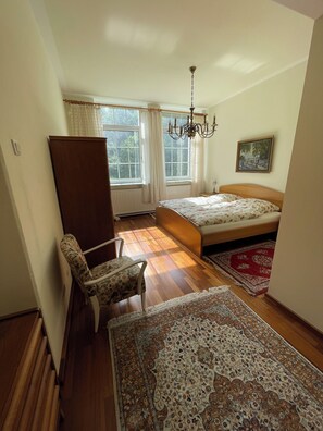 Una camera da letto con un letto, una sedia, un tappeto grande, una finestra con tende e un quadro appeso al muro.