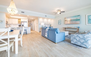 A modern living space with a kitchen, dining area, and a large sofa. - Phoenix Gulf Towers 706 2 Bedroom Condo (Orange Beach)