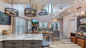 A spacious kitchen with a marble countertop, wooden cabinets, and modern pendant lighting.